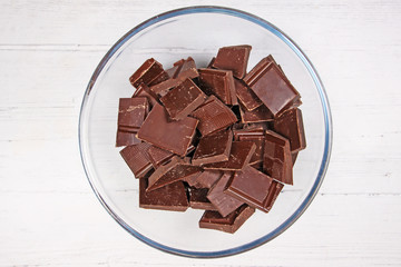 Dark chocolate in a glass bowl on white wood background top view