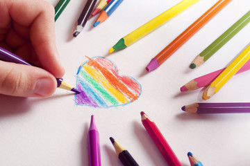 Naklejka premium A child paints a heart with colored pencils in LGBT colors. Children's creativity. Gay-lesbian movement. Same-sex parents. Unisex love.