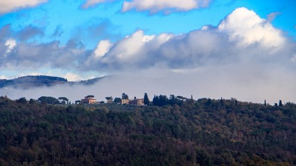 Fototapeta premium Italian pintoresque village in the mountains with fog under cloudy and blue sky