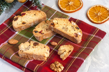 Traditional Italian Biscotti or Cantuccini cookies with hazelnuts, almonds, walnuts on a red-green napkin near the Christmas tree. Christmas and New Year baking.