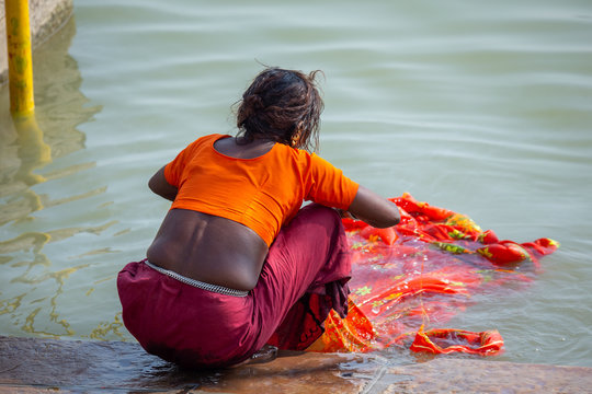 Life on the Ganges: Low caste untouchable indian woman washing a bright orange sari in t he holy river Ganges. Poverty in India.