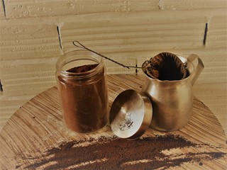 Jarra y envase de cafe con un colador y cafe regado en la mesa