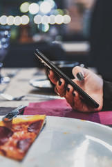 woman hand using mobile phone in cafe with a piece of pizza in plate on table