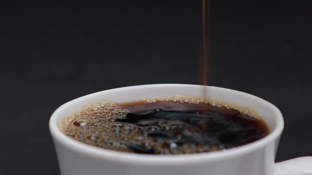 pouring steaming hot black coffee with smoke in to a white cup with beverage drink coffee, black background	