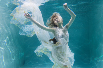 Beautiful blonde girl in a white dress swims underwater in a pool with bubbles. Suitable for...