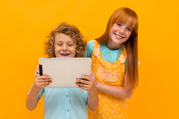 Two happy brother and sister with summer hats are surprised to look at the tablet on a yellow background