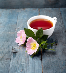 Rosehip flowers and cup of healthy tea, herbal medicine. A cup of  tea with rosehip on the wooden background.