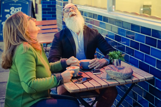 Hipster Retired Senior Couple In Love Drinking Hot Cappuccino At Outdoor Cafeteria. Sweet Couple, Laughing For A Joke  - Joyful Elderly Lifestyle Concept With Wife And Husband. Image