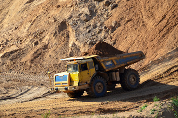 Big yellow dump truck transporting sand in an open-pit mining quarry. Mining quarry for the production of crushed stone, sand and gravel for use in the construction industry - image