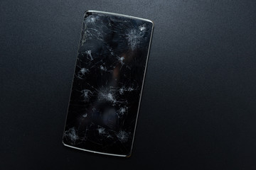 A broken phone on black background. Crushed device with broken screen representing an accident. Textured screen with damage. Dark glass of a screen, broken.