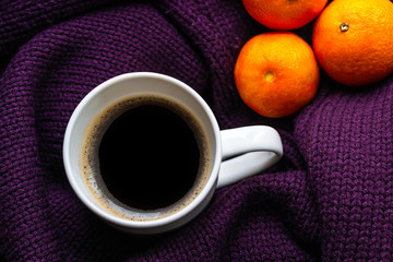 Tangerines and cup of coffee on a warm purple knitted sweater. Concept of winter moon and new year and christmas time