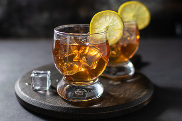 Two glasses of scotch or bourbon with ice and lime on the wooden tray on dark vintage background. Party drinks concept.