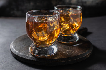 Two glasses of bourbon or rum with ice on dark background close up. Party drinks concept.