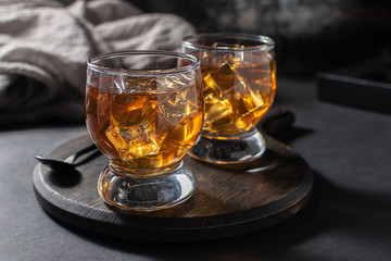 Two glasses of Scottish whiskey or bourbon with ice on the wooden tray. Party drinks concept.