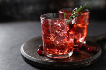 Two glasses of refreshing alcoholic cocktail with vodka or rum, cranberry juice, ice and rosemary on dark background. Party drinks concept. 