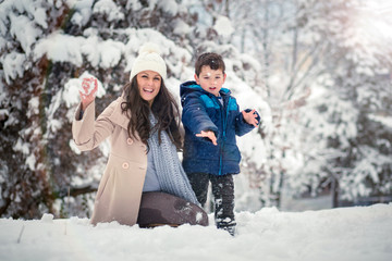 Fototapeta na wymiar Beautiful, young mom and her cute son enjoying winter, playing with snow
