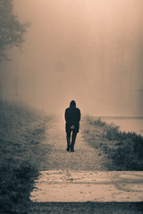 Old man walking down a path next to a foggy river