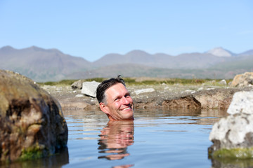 Fototapeta premium Man bathing and relaxing in hot springs during summer day. Natural hot geothermal springs and pool in the Iceland, Europe.