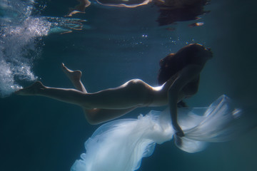 Beautiful girl swims underwater with long hair. Blue or gold background like gold. The atmosphere...