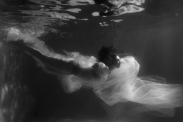 Fototapeta na wymiar Beautiful girl swims underwater with long hair. Blue or gold background like gold. The atmosphere of a fairy tale or magic. Diving under the water with a shiny cloth