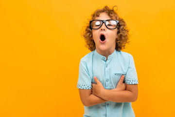 Red-haired curly boy in glasses and a light blue T-shirt crossed his arms and screaming on a yellow...