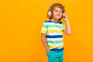 Red-haired curly boy listens to music in large headphones on a yellow background