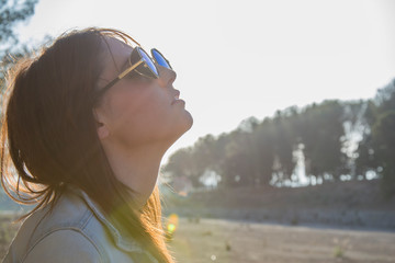 chica joven de perfil con gafas de sol con el sol de fondo