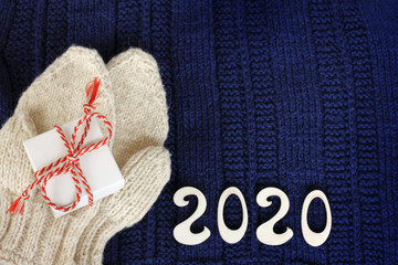 gift with mittens and numbers 2020 on a knitted blue sweater top view. warm winter holidays