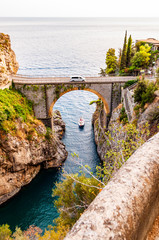 View on Fiordo di Furore arc bridge built between high rocky cliffs above the Tyrrhenian sea bay in Campania region. Car driving on the bridge, boat floating by the unique cove under