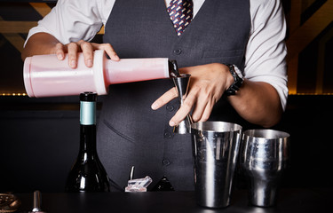Closeup of man hands pouring alcoholic drink in to a jigger to prepare a cocktail. Barman preparing the cocktail at the bar counter..