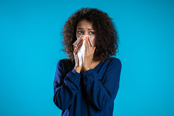 Young girl with afro hair sneezes into tissue. Isolated woman is sick, has a cold or has allergic reaction. Health, medicine, illness, treatment concept - obrazy, fototapety, plakaty