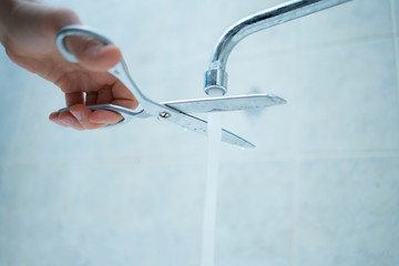 stop wasting the pure water, hand with scissors cut the water stream from faucet at home,...