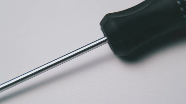 motion past new crosshead screwdriver with red and black handle lying on light surface extreme close view