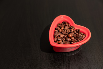 In love with coffee. Coffee is in my heart. Coffee beans in heart shaped bowl on the black desk.