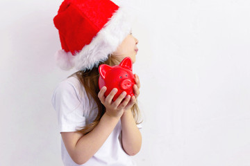 Young child girl in a Santa hat keeps a piggy Bank isolated.