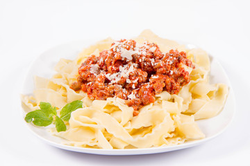 Reginette pasta with bolognese sauce decorated with parmesan and fresh herbs on a plate on a white background