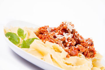 Reginette pasta with bolognese sauce decorated with parmesan and fresh herbs on a plate on a white background
