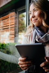 Fototapeta premium Beautiful Asian woman with tablet in her hands looking through the window