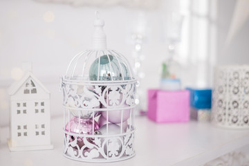 Christmas toys balls silver blue pink in white openwork cage on the background of Christmas lights.
