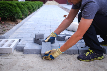 The master in yellow gloves lays paving stones in layers. Garden brick pathway paving by...