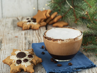 Christmas homemade gingerbread cookies, and a glass cup with hot cappuccino coffee. Close-up. Wooden vintage background, near the branches of spruce.