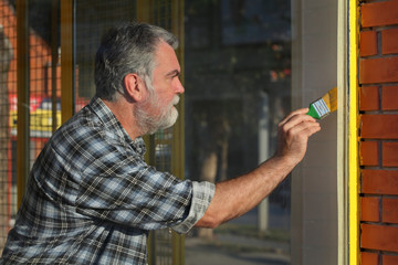 Worker painting metal window to yellow color