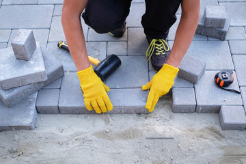 The master in yellow gloves lays paving stones in layers. Garden brick pathway paving by...