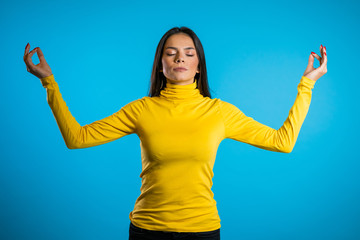 Calm girl in yellow relaxing, meditating. Woman calms down, breathes deeply with mudra om and shut eyes.