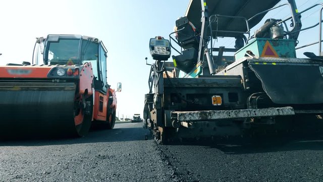 Fresh asphalt road with paving machines in a front view. Road construction process.