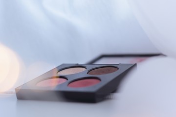 Closeup of eyeshadow palette with fairy lights in the foreground. Concept of winter makeup.