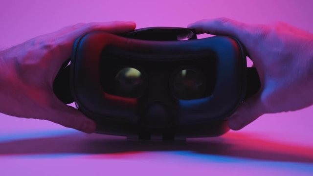 Mans hands take vr glasses wear them at red and blue background. Virtual reality mask. Close-up in 4K, UHD