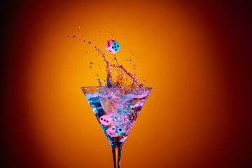 Dice fall in a glass of martini. Colourful cocktail in glass with splash.