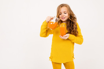 young girl pours carrot juice from a jug into a glass on a white background