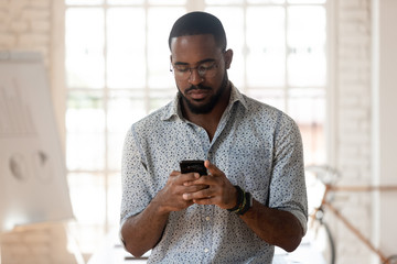 Serious african american young employee using smartphone.